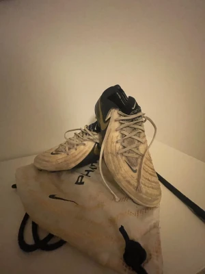 Nike Phantom Vision fotbollsskor vita elite - Säljer ett par Nike Phantom Vision fotbollsskor i vitt med svarta detaljer och snörning. Skorna har en modern design med stickad ovandel och högre krage för extra stöd. Perfekta för dig som vill ha kontroll på planen. Medföljer originalpåse.