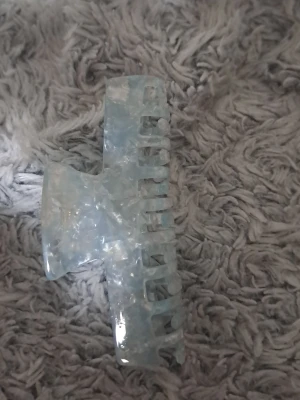 Isblå hårklämma i akryl - Säljer en snygg isblå hårklämma i genomskinlig akryl med marmorerad effekt. Klämman har en klassisk rektangulär form och passar perfekt för att hålla upp håret på ett stilrent sätt. Superenkel att använda och ger en fräsch look.