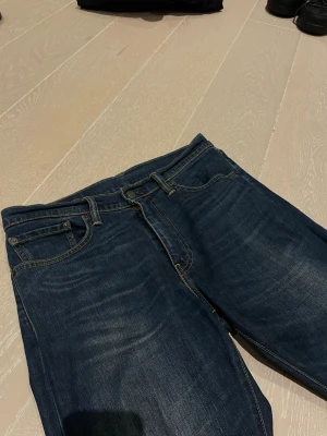 Mörkblå slim fit jeans - Snygga mörkblå jeans med slim fit passform och klassisk femficksdesign. Jeansen har subtila slitningar och kontrastsömmar för en modern look. Perfekta till sneakers eller boots och passar till det mesta i garderoben.