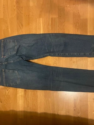 Blå jeans från Levi's - Klassiska blå jeans från Levi's med rak passform. Jeansen har en tidlös look med subtila slitningar och är tillverkade i denim. Perfekta för en avslappnad och stilren vardagsstil. Slitning på vänster lår syns på bild 4.