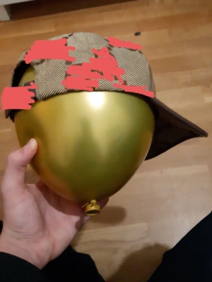 Brun-beige keps  - Snygg keps i brun-beige rutigt tyg med böjd skärm och justerbart spänne bak. Kepsen har en klassisk form och är fodrad med svart tyg på insidan. Perfekt accessoar för en stilren och avslappnad look.