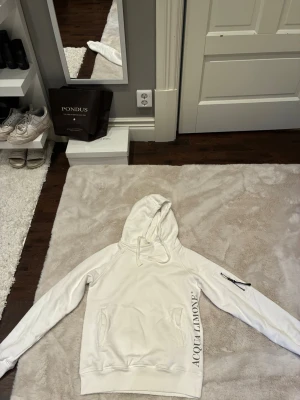 Vit hoodie från Acqua Limone - Snygg vit hoodie från Acqua Limone med stor gul citronlogga på ryggen och text på ena ärmen. Hoodien har huva, fickor framtill och en dragkedjeficka på ena ärmen. Perfekt för en avslappnad och trendig stil.