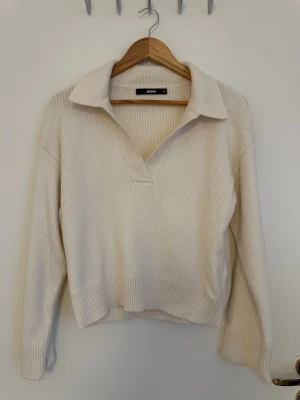 Vit ribbstickad tröja med krage - Säljer en vit ribbstickad tröja från Bik Bok med snygg krage och v-ringning. Tröjan har lång ärm och avslappnad passform, perfekt för en chill och stilren look. Materialet är mjukt och stretchigt för extra komfort.