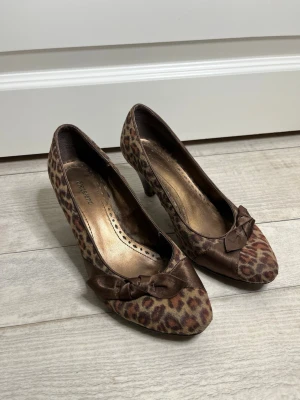 Leopardmönstrade pumps med rosett - Snygga pumps i storlek 36 men passar också 37. Från Graceland med leopardmönster i brunt och beige. Skorna har spetsig tå och en dekorativ brun rosett framtill. Materialet är textil med satinkänsla och klacken är medelhög. Perfekta för dig som gillar djurmönster och vill sticka ut.