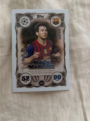Magic Memories fotbollskort Messi - Samlarfotbollskort från Topps med Lionel Messi i Barcelona-tröja. Kortet har texten 'Magic Memories' och visar statistik samt klubbmärke. Färgerna är blå, röd och guld med detaljerad ram och UEFA Champions League-symbol.