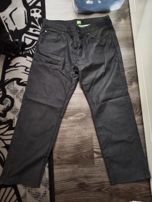 Svarta raka jeans från Hugo Boss  - Säljer ett par svarta jeans från Hugo Bossmed rak passform och klassisk femficksdesign. Jeansen har bälteshällor och knappgylf. Materialet är denim i bomull och de har en stilren look som passar till det mesta.