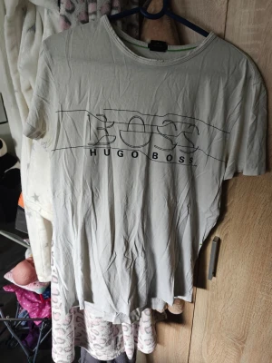 Vit Hugo Boss t-shirt med tryck - Vit t-shirt från Hugo Boss med stort svart tryck på bröstet där det står 'BOSS HUGO BOSS'. Klassisk rund halsringning och korta ärmar. Perfekt för en stilren och enkel look. Tyvärr några fläckar här och där kan gå bort men vet ej 