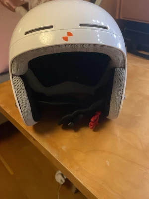 Vit hjälm från POC med autografer - Säljer en vit hjälm från POC med blå logga på sidan och autografer på ovansidan. Hjälmen har ventilationshål, mjuk grå inredning och justerbart hakspänne med röd detalj. Perfekt för dig som vill sticka ut i backen. Den är använd och har lite repor. Men funkar parfekt 