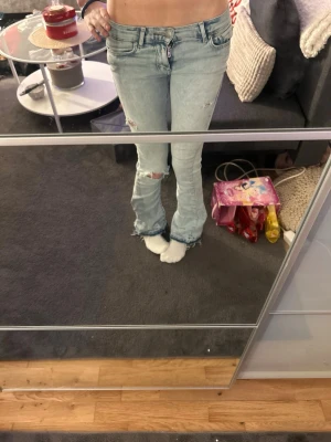 Ljusblå slitna bootcut jeans - Säljer ett par ljusblå bootcut jeans med slitningar på knäna och låg midjade sytt upp på längden, sytt dom låg midjade och gjort hål väldigt snygga 