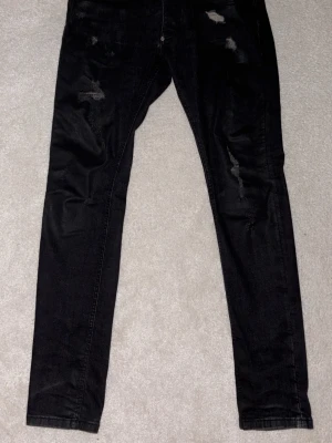 Svarta slitna skinny jeans philipp plein  - Säljer ett par svarta skinny jeans med slitningar på både fram- och baksida. Jeansen har klassisk femficksdesign och är tillverkade i stretchigt denimtyg för en tajt passform. Perfekta för en trendig och avslappnad look.