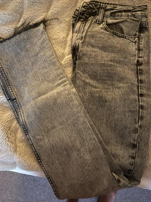 Gråa raka jeans med rå kant - Säljer ett par gråa jeans med rak passform och rå, fransig kant vid bensluten. Jeansen har klassisk femficksdesign och bälteshällor. Perfekta för en avslappnad och trendig look.