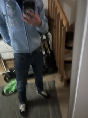 Babyblå Von studio hoodie med bling - Säljer en babyblå hoodie från Von studio med dragkedja, huva och fickor framtill. På bröstet finns blingade bokstäver och en cool tecknad figur. Hoodien har snören i huvan och är perfekt för dig som gillar streetwear och vill sticka ut.