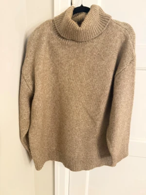 Beige stickad polotröja - Mysig beige stickad polotröja med bred krage och avslappnad passform. Tröjan har långa ärmar, ribbade muddar och nederkant. 