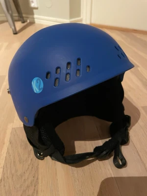 Blå hjälm från K2 - Säljer en blå hjälm från K2 med ventilationshål och justerbart hakband. Hjälmen är tillverkad i hårdplast med mjuk vaddering på insidan för extra komfort. Passar huvudomfång 51-55 cm och har svart innerfoder.