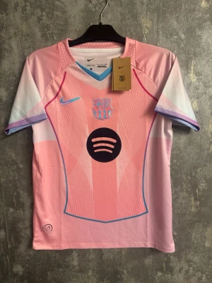 Barca x Nike rosa fotbollströja - Storlek S - Säljer en limited edition FC Barcelona x Nike matchtröja i rosa och pastellfärger. Tröjan har ett holografiskt Barça-märke, blå Nike-logga och Spotify-logga på bröstet. Tillverkad i lätt polyester med coola grafiska detaljer och korta ärmar.