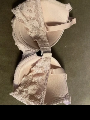 Ljusrosa spets-bh med vaddering - Söt ljusrosa bh med vadderade kupor och fina spetsdetaljer längs kanterna. Justerbara axelband och hakknäppning bak. Perfekt för dig som gillar en feminin och stilren look. Storlek 75E