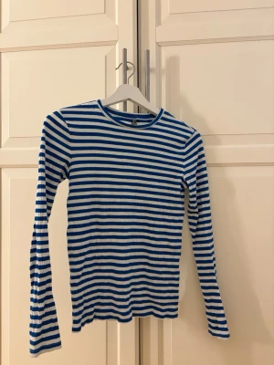 Randig långärmad topp från Pieces - Säljer en ribbad långärmad topp från Pieces i storlek XS. Toppen har blå och vita horisontella ränder och är tillverkad i ett mjukt, stretchigt material. Perfekt till jeans eller kjol för en avslappnad look.