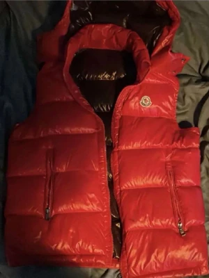 Röd dunväst från Moncler - Säljer en röd dunväst från Moncler med glansig finish. Äkthetsintyg saknas då den är köpt här på Plick. Använt skick därav det lägre priset! Hör av er vid frågor!