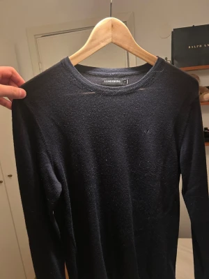 Mörkblå stickad tröja J.Lindeberg - Snygg mörkblå stickad tröja från J.Lindeberg i storlek M. Tröjan har rund hals och långa ärmar, perfekt för dig som gillar stilrena och klassiska plagg. Materialet är mjukt och skönt, passar bra till jeans eller chinos. Diskret JL-logo på bröstet.