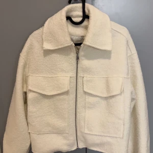 Vit teddyjacka med dragkedja - Säljer en mysig vit teddyjacka med dragkedja framtill och två stora fickor på bröstet. Jackan har en klassisk krage och är perfekt för kyligare dagar. Den är både stilren och bekväm, vilket gör den till ett måste i garderoben.