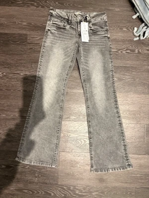 Grå bootcut jeans Gina Tricot - Säljer ett par gråa bootcut jeans från Gina Tricot med snygg tvättad look. Byxorna har fem fickor, bälteshällor och knappgylf. Materialet är klassisk jeans med en mjuk känsla och passformen är normal med utsvängda ben.