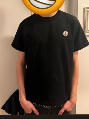 Svart Moncler t-shirt i bomull - Säljer en svart t-shirt från Moncler med klassisk rund hals och korta ärmar. T-shirten har Monclers ikoniska logga broderad på bröstet och är gjord i mjuk bomull. Enkel och clean design som funkar till allt.