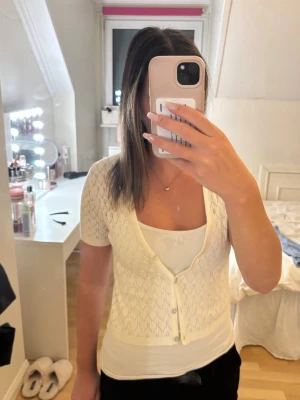Vit stickad kortärmad topp med knappar - Supersöt vit stickad topp/kofta med korta ärmar och pärlknappar framtill. Perfekt att styla över ett linne eller topp för en fräsch look. Den är köpt second hand så det står tyvär inget märke. Säljer för att den e för liten därför aldrig använd av mig själv. Storlek S/Xs