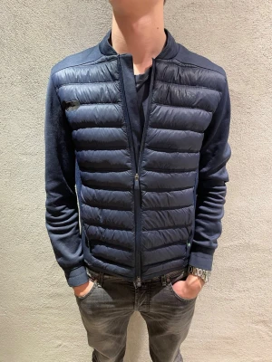 Hugo boss cardigan  - Snygg mörkblå pufferjacka från BOSS med quiltad front och släta ärmar. Jackan har dragkedja framtill och diskret BOSS-logga på bröstet. Perfekt för dig som vill ha en stilren och modern look. Passar till både jeans och sneakers.