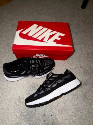 Nike P-6000 - Nike sneakers i svart och vitt med meshpaneler och snygga detaljer. Skorna har snörning, platt sula och rund tå. Swoosh-loggan syns tydligt på sidan och sulan har ett coolt mönster. Perfekta för dig som gillar sportig och modern stil.