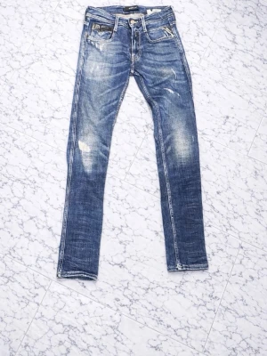 Replay blå jeans, modell 914L - Säljer ett par snygga Replay jeans i klassisk blå tvätt med slitningar och coola detaljer. Modellen är 914L med raka ben och skinny passform. Jeansen har fem fickor, tydliga sömmar och läderpatch bak i midjan. Perfekt för dig som gillar street och casual stil. Hör av vid funderingar!