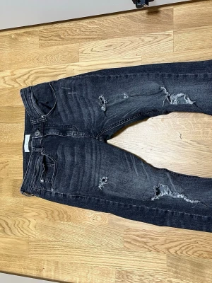 Mörkblå slitna jeans från Pier One - Säljer ett par mörkblå jeans från Pier One med snygga slitningar och distressed detaljer på benen. Klassisk femficksmodell med raka ben och normal passform. Materialet är en mjuk och stretchig bomullsblandning som sitter skönt hela dagen. de är storlek 28/30