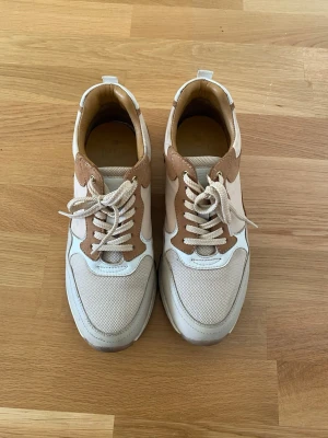 Beige och vita sneakers från Dasia - Snygga sneakers från Dasia i beige och vitt med detaljer. Skorna har snörning, rund tå och en rejäl sula för extra komfort. Perfekta för dig som gillar stilrena och neutrala färger. Storlek 41 men passar även någon med storlek 40 