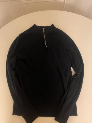 Svart quarter zip stickad tröja Jack & Jones - Svart stickad tröja från Jack & Jones med half zip och ringdetalj på dragkedjan. Tröjan har ribbade muddar vid ärmslut och nederkant samt en hög krage. Perfekt för dig som gillar enkel och stilren design.