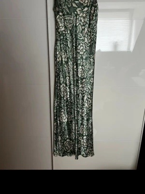 Grön långklänning med blommönster - Säljer en grön mönstrad  långklänning med  blommönster. Oanvänd