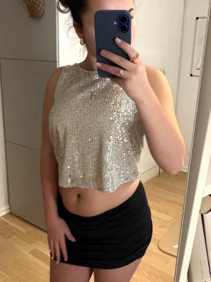 Glittrig croppad topp från Lindex - Säljer en glittrig croppad topp från Lindex i silver med paljetter. Toppen är ärmlös och har en rak, lös passform som ger en snygg och trendig look. Perfekt för dig som vill sticka ut och glänsa lite extra.