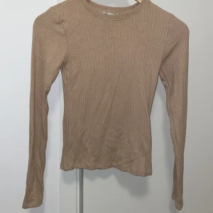 Beige ribbad långärmad tröja New Yorker - Säljer en beige ribbad långärmad tröja från FB Sister. Tröjan har en rund halsringning och är figurnära i modellen. Perfekt att styla med jeans eller kjol för en enkel och snygg look.