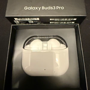 Galaxy Buds3 Pro - Samsung Galaxy Buds3 Pro i vitt, komplett med originalförpackning. Trådlösa hörlurar med modern design och laddningsetui. Produkten ser ut att vara i nyskick utan synligt slitage eller defekter. Perfekt för musik, samtal och träning med hög ljudkvalitet.