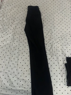 Svarta bootcut kostymbyxor - Snygga svarta kostymbyxor med bootcut passform och klassiska hällor för bälte. Högmidja! Byxorna har en stilren look och är tillverkade i ett slätt tyg som känns dressat. Perfekta för dig som gillar en tidlös och clean stil.