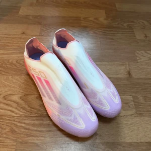 Lamine Yamal F50 fotbollskor  - Säljer ett par Adidas F50 fotbollsskor i en snygg mix av vitt, ljusrosa och lila. Skorna har en strömlinjeformad design utan snörning, med platt sula och mönstrad ovandel i syntetmaterial. Perfekta för dig som vill sticka ut på planen med stil. Helt nya inte använda, priset kan diskuteras 😁