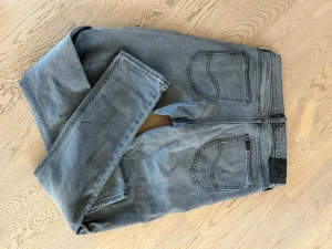 Grå Lee Luke jeans W30 L32 - Snygga grå jeans från Lee, modell Luke, med klassiska bakfickor och svart Lee-lapp bak i midjan. Jeansen har raka ben och är tillverkade i bomull med en skön passform. Perfekta för dig som gillar en stilren och enkel look.