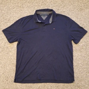 Marinblå Tommy Hilfiger pikétröja  - Klassisk snygg marinblå pikétröja från Tommy Hilfiger i storlek XXL, men skulle nog säga den passar mer som XL/L. Använd fåtal gånger och skicket är i princip som ny, inga defekter eller slitningar. Passar superbra för dig som gillar en mer elegant stil. Skick: 8.5/10