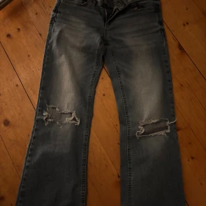 Blå ripped jeans från Nelly - Snygga blå jeans från Nelly med slitna detaljer och hål vid knäna. Modellen har bootcut och klassiska fickor med lock och knapp bak. Jeansen har en cool tvättad look och är tillverkade i jeansmaterial. Dessa är extremt oanvända vilket gör att dom är i toppskick, kom privat för mer bilder eller diskussion av pris!💞