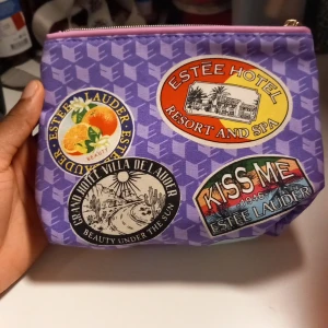 Lila necessär från Estée Lauder - Superfin lila necessär från Estée Lauder med coola retroinspirerade tryck och patchar i olika färger. Väskan har dragkedja upptill och är perfekt för smink eller småprylar. Tillverkad i syntetmaterial med geometriskt mönster och färgglada detaljer. Innehåller en 30ml Take It Away Makeup Remover Lotion, en 7ml Revitalizing Supreme+ Global Anti-Aging Cell Power Creme, en 5ml Revitalizing Supreme+ Global Anti-Aging Power Eye Balm, och ett läppstift i färgen Envy.