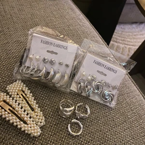 Set med örhängen, ringar och pärlspännen - Säljer ett komplett smyckeskit med två paket silvriga örhängen i olika former, tre chunky silverringar och två hårspännen dekorerade med vita pärlor och guldiga detaljer. Perfekt för dig som gillar att mixa och matcha accessoarer. Jag har aldrig använt som ni ser och köpte allt för 350 kr 