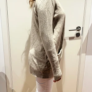 Beige kofta från Vila med fickor - Snygg beige kofta från Vila i mjukt stickat material. Modellen är öppen framtill och har två praktiska fickor samt ribbade muddar vid ärmslut och nederkant. Perfekt att slänga över en t-shirt eller linne för en chill look.