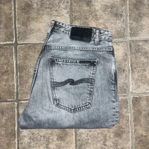 Nudie Jeans  - Snygga grå jeans från Nudie Jeans i modellen Breezy Britt. Jeansen har klassisk femficksdesign, raka ben och hög midja. Tillverkade i 100% ekologisk bomull med cool tvättad look och svarta detaljer på bakfickorna. Midja 41cm, längd 106cm. JAG SKICKAR EJ FLER BILDER NÄR JAG BÄR JEANSEN! för storleksguide hänvisar jag till måtten och för bättre inblick i passformen rekommenderar jag att googla på modellnamnet. Jeansen kan vara uppsydda utan att jag noterat det så kolla måtten noggrant :) s4 