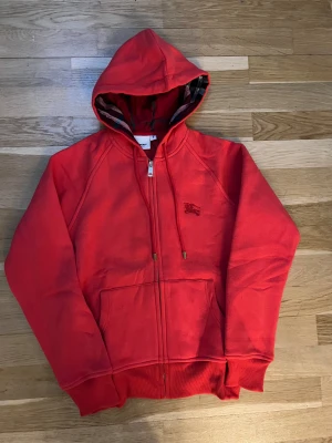 Röd hoodie från Burberry  - Helt ny och superpopulär tröja! Perfekt för dig som söker julklapp till en tjej 150-170cm/40-60kg Aldrig använts, i nyskick. Tröjan är tjock, varm och perfekt för vintern, bäde för en fin och bekvam look. Tröjan är för kvinnor. modellen ar tajtare vid midjan. Saljer den pa grund av storleken. Den ar i storlek S, men passar battre som XS. Hör gärna av dig om du har nägra fragor eller funderingar!