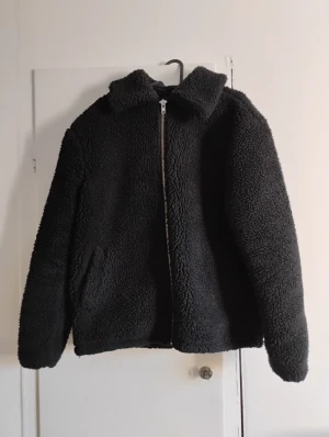 Svart jacka från T.T i S - Svart jacka från T.T i storlek S. Jackan har fluffig och mjuk yta, klassisk krage och dragkedja framtill. Två sidofickor och helsvart färg gör den enkel att matcha. Perfekt för dig som gillar chill och comfy stil.