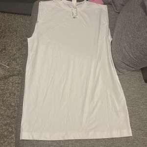 Vit ärmlös klänning från H&M - Oversized Vit, enkel och stilren klänning från H&M i storlek M. Modellen är ärmlös med rund hals och rak passform, perfekt för dig som gillar minimalistisk stil. Materialet är mjukt och lätt, vilket gör den skön att bära under varma dagar.