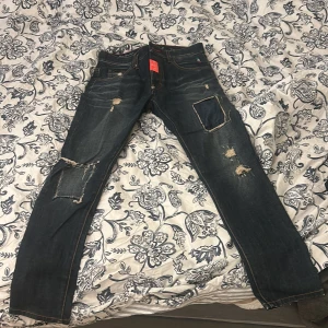 Philipp Plein  jeans med slitningar - Säljer ett par mörkblå  jeans från Philipp Plein i storlek 30. Jeansen har coola slitningar och patch-detaljer på benen, klassiska fem fickor och kontrastsömmar. Perfekt för dig som gillar  streetstyle och vill sticka ut med din look.